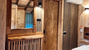 Una habitación de madera con un espejo integrado, un equipo de aire acondicionado y una cama con cabecera blanca.