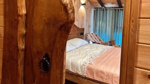 Interior de una cabaña de madera con una cama, un sillón y una puerta de madera.