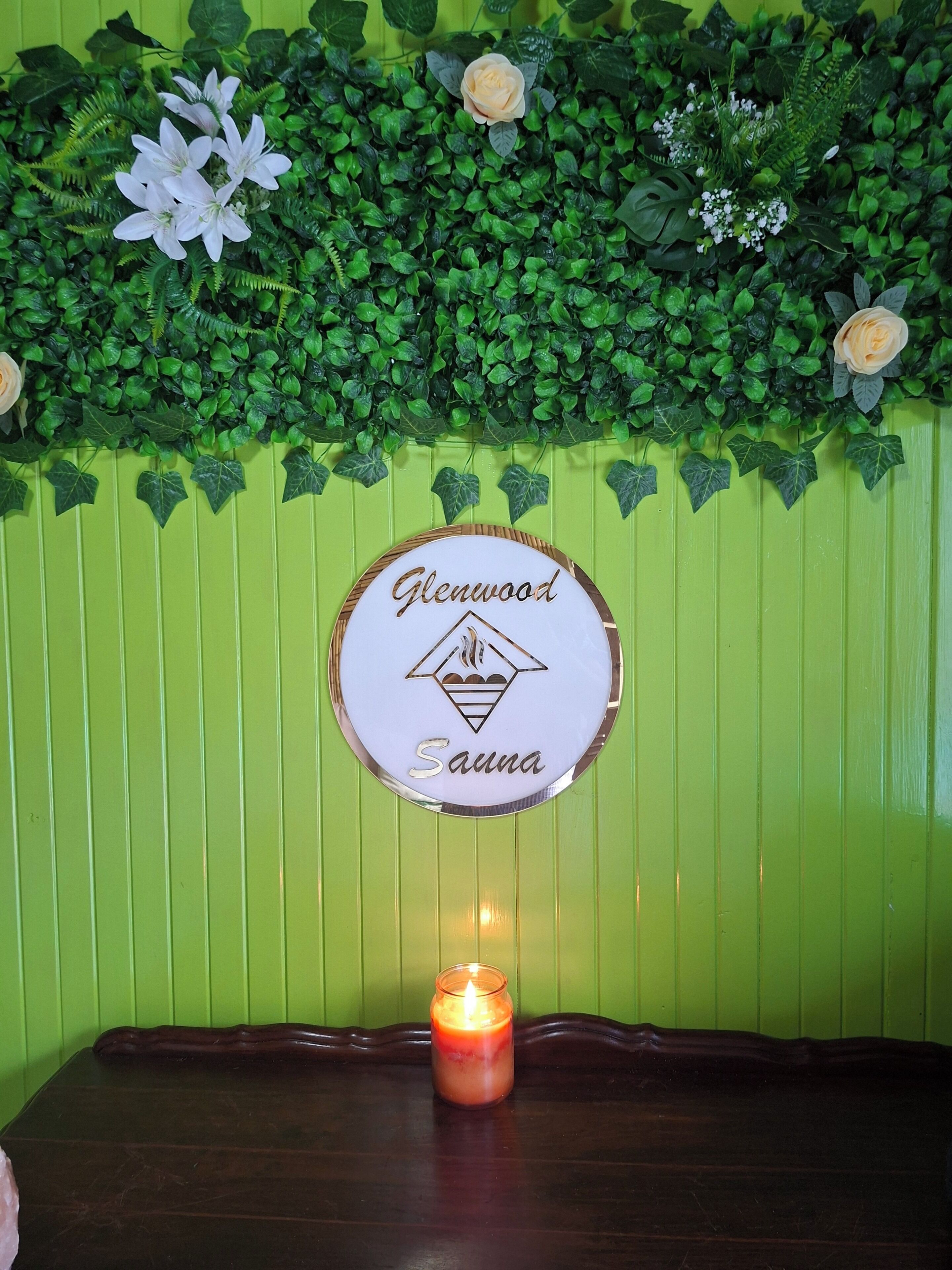 A wall with a sign reading 'Glenwood Sauna' and a lit candle on a wooden table.
