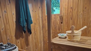 A wooden cabin interior with a stone floor, a wooden table with a bowl and spoon, a green towel hanging, and a window with a view of greenery. - Quaint cottage in Glenwood, Durban (Durban)