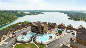 A hotel with a swimming pool, parking lot, and a view of a lake.