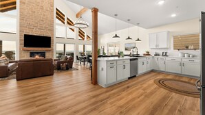 A spacious living area with a fireplace, a dining area, and a kitchen with white cabinets and a wooden floor.