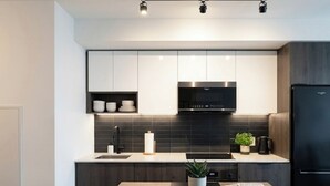 A modern kitchen with dark cabinetry, a stainless steel range hood, and a black refrigerator.