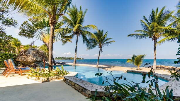A pool area with lounge chairs and palm trees, overlooking the ocean. - Beachfront Combo Villa with Pool & Spacious Layout (North Placencia)