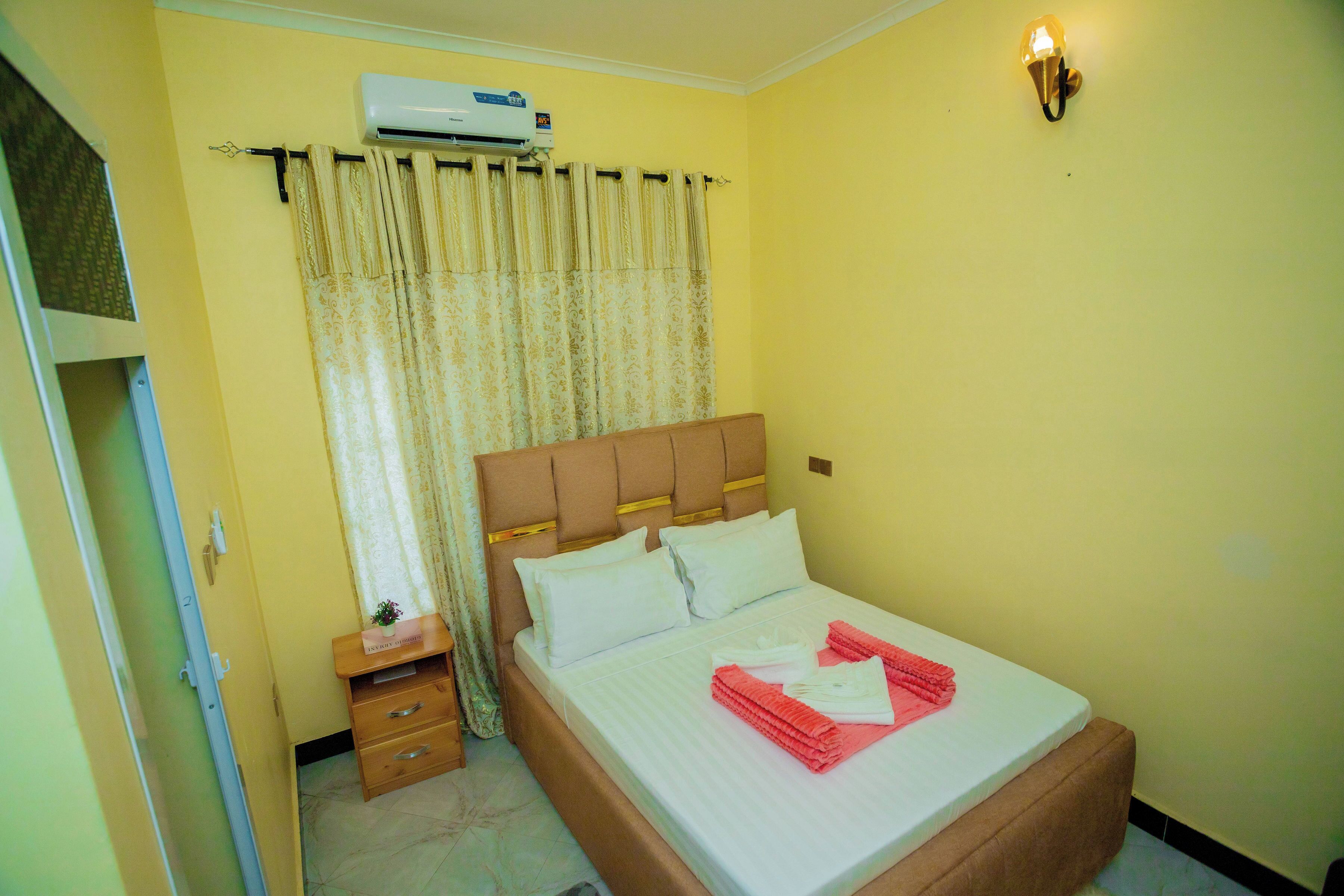 Habitación de hotel con cama, mesita de noche, cómoda, equipo de aire acondicionado y lámpara fijada a la pared.