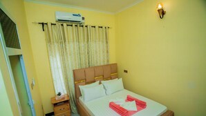 Une chambre d’hôtel comprenant un lit, une table de chevet, une commode, un appareil de climatisation et un luminaire fixé au mur.