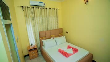 Habitación de hotel con cama, mesita de noche, cómoda, equipo de aire acondicionado y lámpara fijada a la pared.