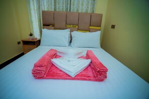 A neatly made bed with pink and white towels, a wooden nightstand with a book and a small plant, and a headboard with a gold accent.