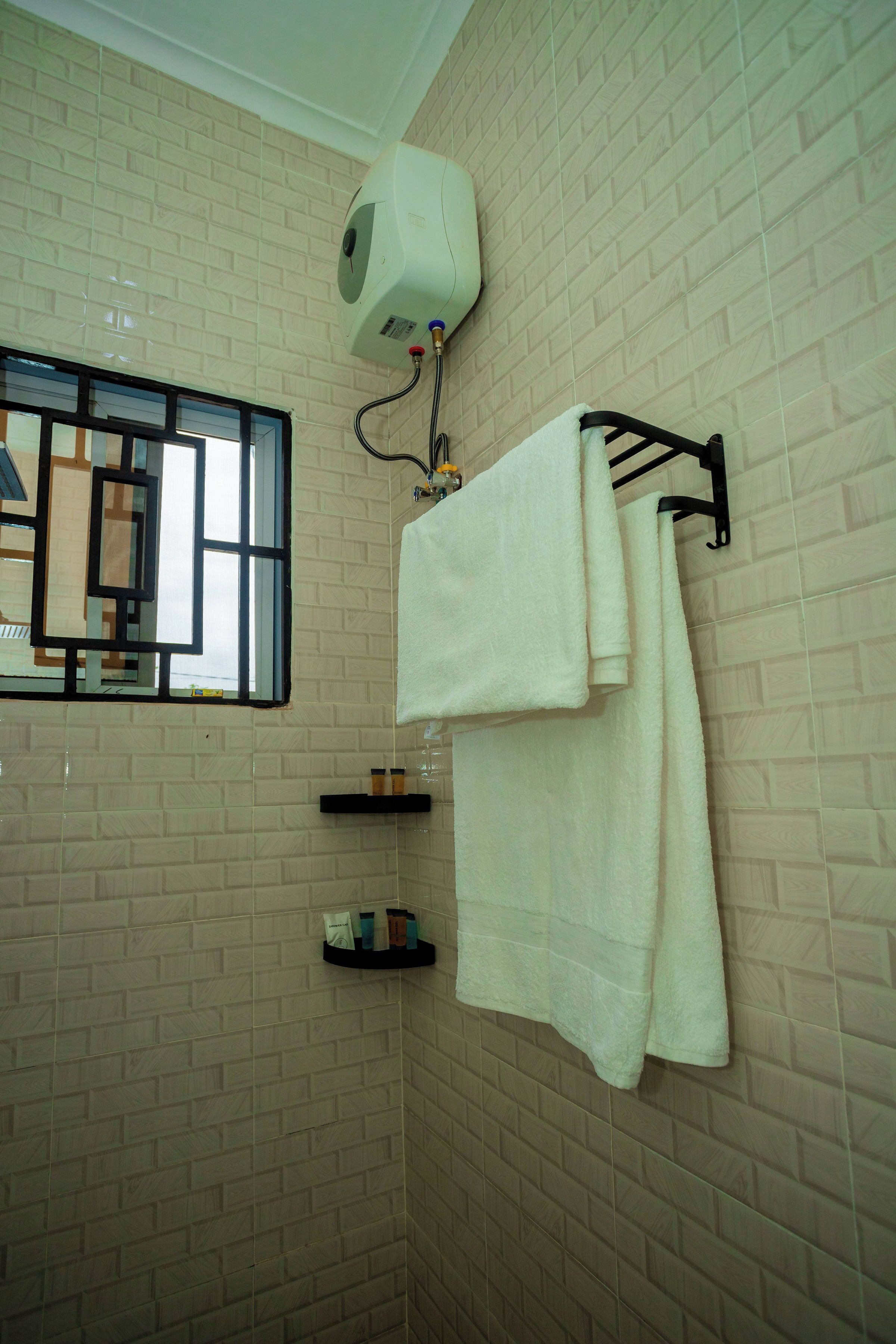A bathroom with a tiled wall, a window with bars, a towel rack with towels, and a shelf with toiletries.
