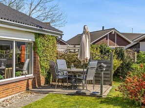 Eine Terrasse mit Tisch und Stühlen, einem Sonnenschirm und einer Ziegelwand mit Kletterpflanzen.