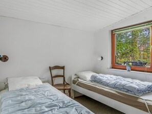 Ein Zimmer mit zwei Einzelbetten, einem Holzstuhl, einem Fenster mit Blick auf Bäume und einer Wandlampe.
