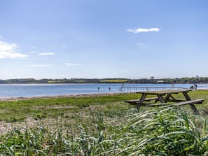 Picnicområde ved søen med træbænk, en anløbsbro der stikker ud i vandet, og et fjerntliggende udsigt over et bakket landskab.