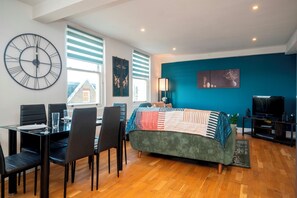 Un salon moderne comprenant un grand lit, une table à manger avec des chaises, un téléviseur et une grande horloge murale.