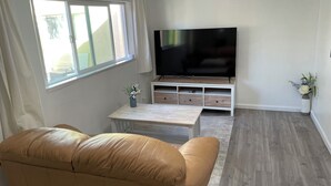 A living room with a leather sofa, a TV on a wooden stand, a small table with a vase, and a window with curtains. - Your own little house.#D Pet-Friendly (Phoenix)