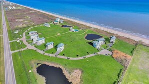 An aerial view of a coastal property with multiple buildings, a large green lawn, and a beach. - Luxury Beachfront Ocean Views Pool Access Sleeps 15 (Bolivar Peninsula)