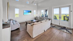 A spacious living room with a large window, a ceiling fan, and a view of the ocean. - Luxury Beachfront Ocean Views Pool Access Sleeps 15 (Bolivar Peninsula)