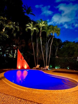 A swimming pool with a geometric sculpture, surrounded by palm trees and lounge chairs. - Coconut Grove Fashion Loft · Pool & Backyard · Walkable (Miami)