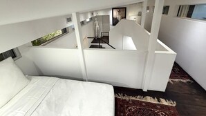 Een moderne slaapkamer met een groot bed, een wit plafond en uitzicht op een trap.