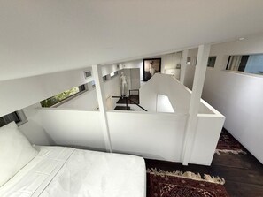 A modern bedroom with a large bed, a white ceiling, and a view of a staircase. - Coconut Grove Fashion Loft · Pool & Backyard · Walkable (Miami)