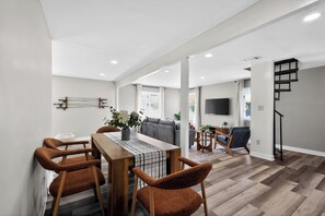 A modern living room with a dining area, a staircase, and a flat-screen TV mounted on the wall. - Infrared Sauna, Firepit, Kayaks, Walk 2 Launch, Authentic WI Lake Life (Poynette)