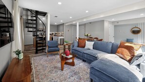 A modern living room with a sofa, coffee table, and a staircase leading to a kitchen. - Infrared Sauna, Firepit, Kayaks, Walk 2 Launch, Authentic WI Lake Life (Poynette)