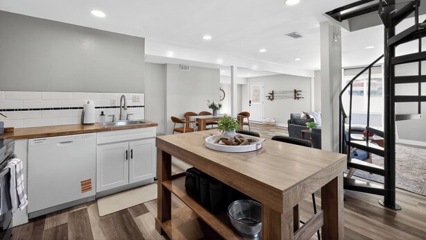 A modern kitchen with white cabinetry, a wooden dining table, and a black spiral staircase. - Infrared Sauna, Firepit, Kayaks, Walk 2 Launch, Authentic WI Lake Life (Poynette)