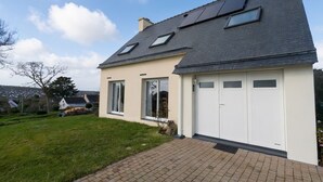 Une maison avec un toit en pente, des panneaux solaires, un garage et une allée pavée.