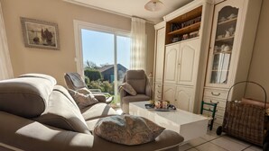 Un salon comprenant un canapé, des fauteuils, une table basse et un buffet contenant de la vaisselle.