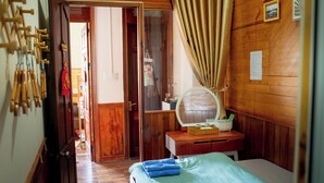 Una habitación de madera con una cama, una mesita de noche con espejo y una puerta que da a otra habitación.