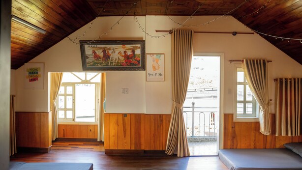 Una habitación con piso de madera, dos camas, un cuadro y una ventana con cortinas.