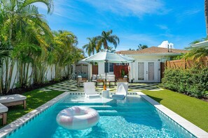 A swimming pool with a checkered pattern, surrounded by palm trees and a covered seating area. - Heated Pool Coastal Retreat Near Beach & Ave (Delray Beach)
