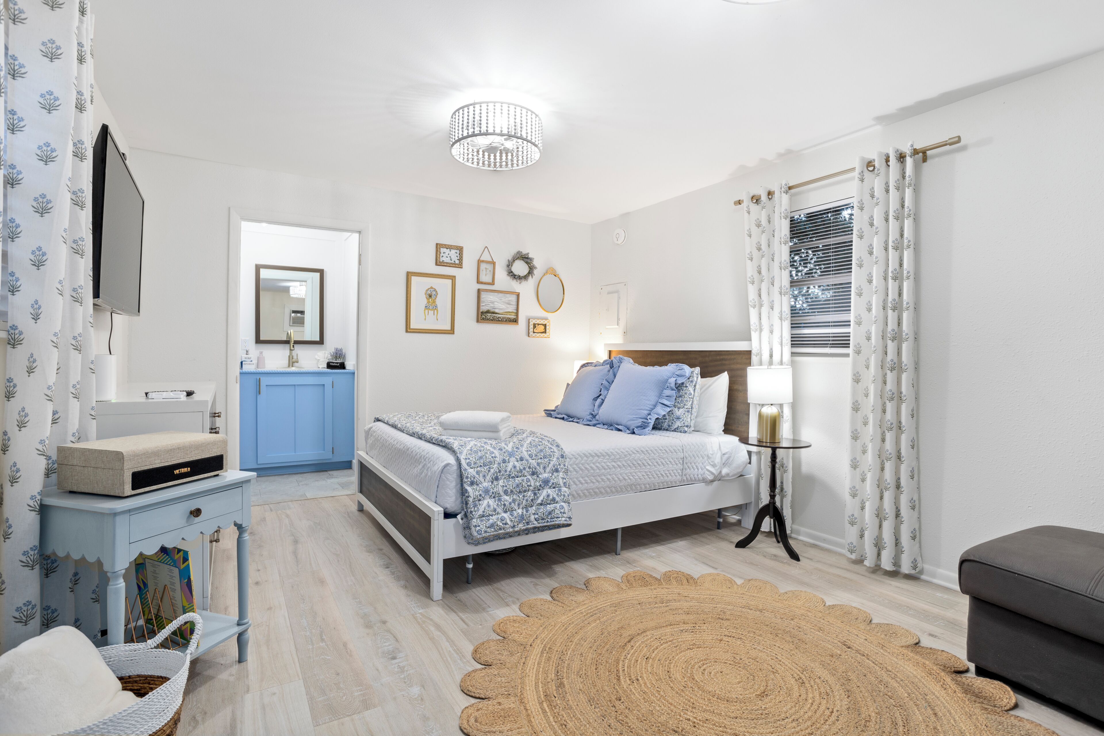 Un dormitorio con cama, mesita de noche, lámpara y una pared decorada con cuadros.