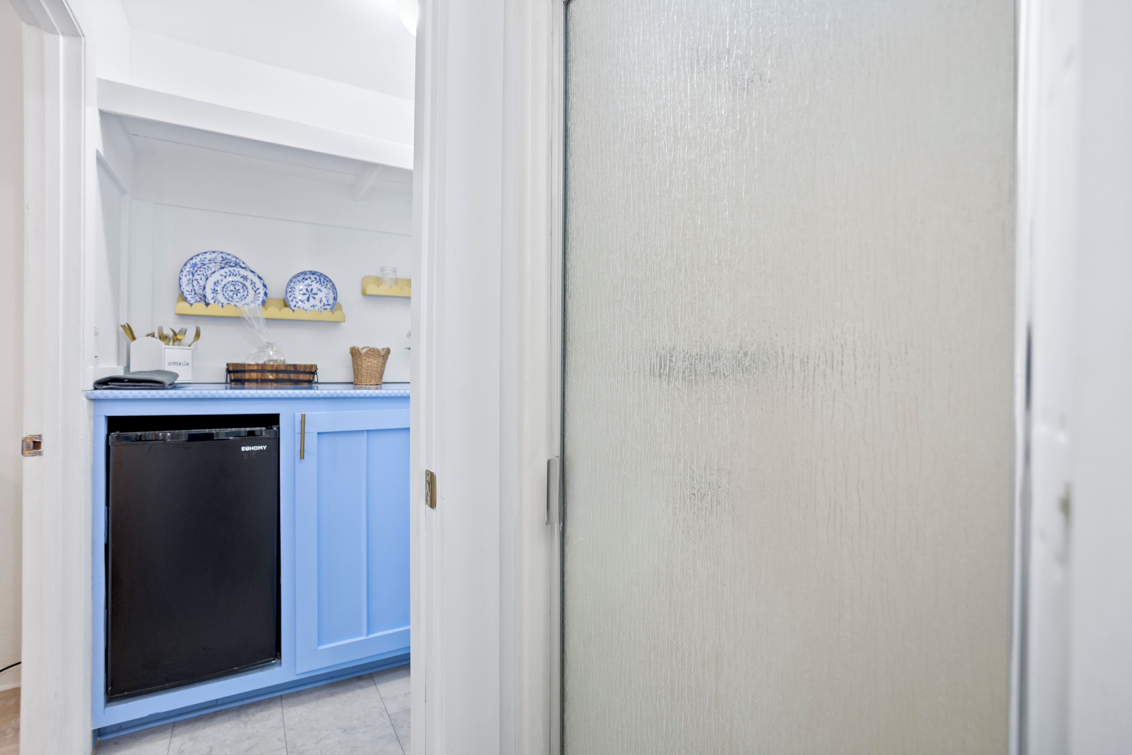 Una cocina con un mueble azul, un lavavajillas negro y platos blancos y azules en una repisa.
