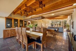 Una habitación amplia con techo de madera, un comedor con mesa de billar y vistas al exterior.