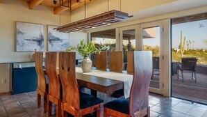 Un coin repas avec une table en bois, des chaises, un vase avec des plantes et une vue sur l’extérieur.