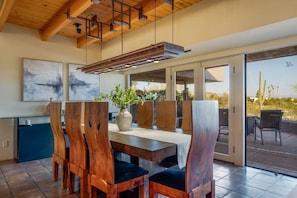Un comedor con una mesa de madera, sillas, un florero con plantas y vistas al exterior.