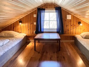 A cozy attic bedroom with wooden walls, a single bed, a small table, and a window with curtains. - 4 Person Holiday Home in Morlunda (Mörlunda)