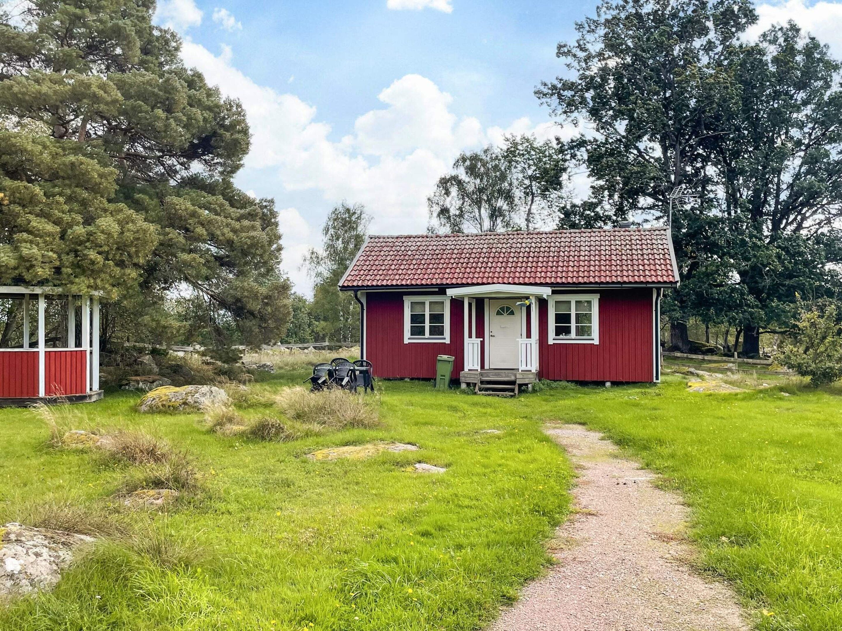 A red house with a porch, a gravel path leading to it, and a small shed to the left.