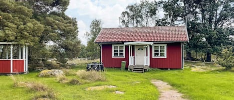 A red house with a porch, a gravel path leading to it, and a small shed to the left.
