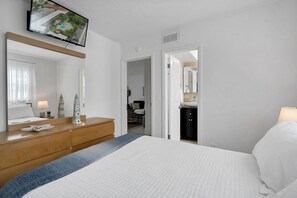 A hotel room with a bed, a dresser, a mirror, a television, and a bathroom visible through an open door. - Coastal Beach Retreat, Heated Pool, Walk to Beach, Water Taxi (Pompano Beach)