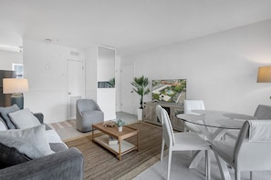 Ein modernes Wohnzimmer mit Sofa, Sessel, Couchtisch, Esstisch, Stühlen und einem Bild an der Wand.