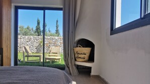 Un dormitori amb un llit gran, vistes a l'exterior, una paret de pedra i una cistella de vimet amb la inscripció 'Alicia Nomade'.