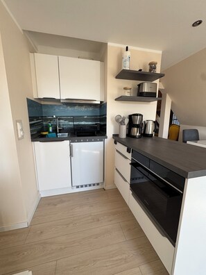 A compact kitchen with white cabinets, a black countertop, and a built-in oven. - Vacation Rental Near the Beach with a Balcony in the Town Center (Ahrenshoop)