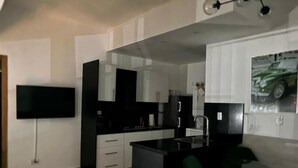 A modern kitchen with a black countertop, white cabinets, and a green chair. - Central Suites Tower T&T Rentals (Santo Domingo)