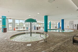 Ein beheiztes Hallenbad mit einer Springbrunnenanlage, gefliestem Boden und blauen Säulen.