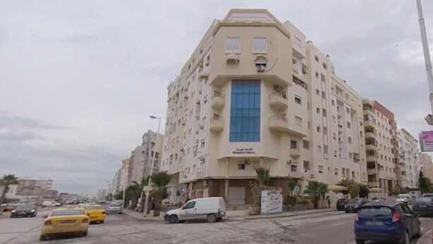 A multi-story hotel with a central blue entrance, multiple balconies, and a parking area with cars. - Luxury & Fully Equipped | Safe & Terrace | All Amenities within Walking Distance (Tunis)