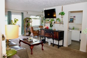 A living room with a sofa, coffee table, TV, and a kitchen area with a sink and cabinets.
