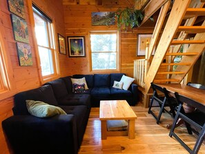 Ein gemütliches Blockhaushaus-Interieur mit einem dunkelblauen Sofa, einem Holztisch und einer Holztreppe.