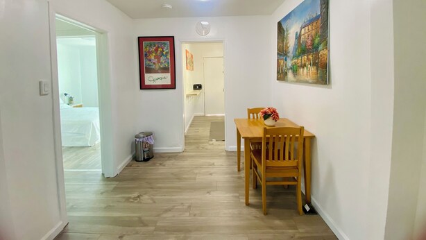Un pasillo con una mesa de comedor y sillas, un cubo de basura, una obra de arte enmarcada y una puerta que da a un dormitorio.