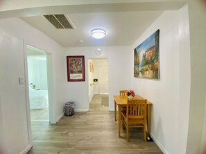 A hallway with a dining table and chairs, a trash bin, a framed artwork, and a door leading to a bedroom. - Tifany blue door cotage with AC in Phoenix E (Phoenix)